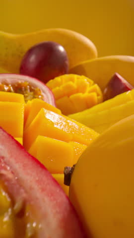 Close-up tropical fruits including juicy sliced mango passion fruit and whole ripe fruits on yellow background. Vertical close-up slow motion