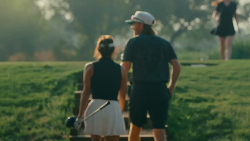 Couple walks slowly upstairs to the tee box in golden hour light after their playing partner hits a drive in the background. A cinematic moment capturing course atmosphere and relaxed game flow.