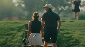 Couple walks slowly upstairs to the tee box in golden hour light after their playing partner hits a drive in the background. A cinematic moment capturing course atmosphere and relaxed game flow. - Powered by Shutterstock - Get 15% off with code: PIKWIZARD15