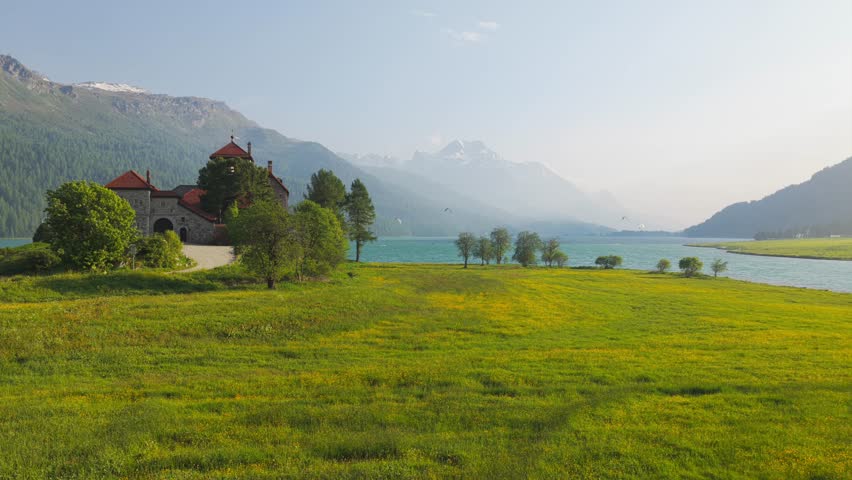 Serene lake surrounded by mountains, cottage, and lush meadow in a tranquil setting. Aerial, Push Forward