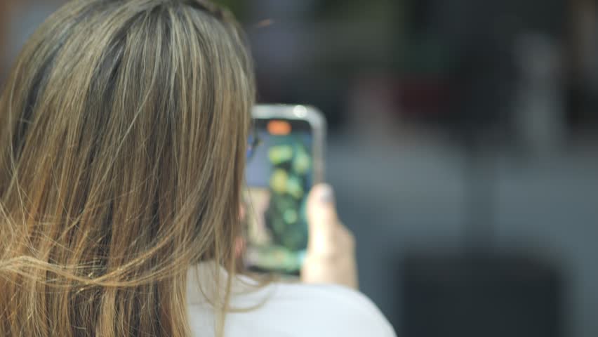 Woman is taking a picture of herself with a cell phone. She is holding the phone up to her face and looking at the camera. Concept of self-awareness and self-expression