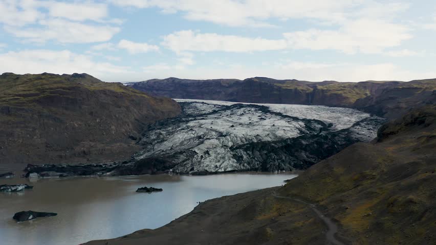 Aerial view of a stunning glacier flowing into a glacial lake, contrasting the stark white ice with the dark, mountainous terrain, Iceland.