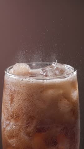 Closeup of sparkling cola drink with ice cubes. Fizzing cola with ice in glass. Refreshing tasty cola drink