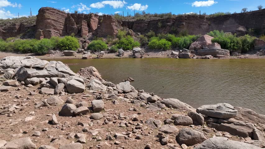 Aerial view of the lake with a rocky shoreline, green shrubbery, and towering rock formations creating a rugged yet serene landscape, Peoria, Arizona, United States.