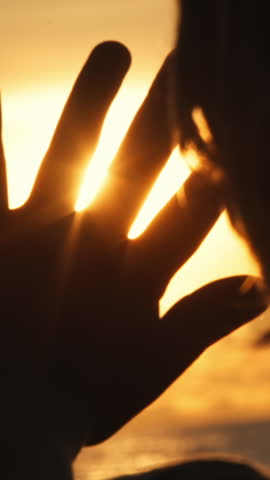 Silhouette of little hand stretching toward ocean sunset, sunlight shining through fingers. Emotional slow motion scene of innocence, freedom, gratitude and peace in beautiful golden hour seaside