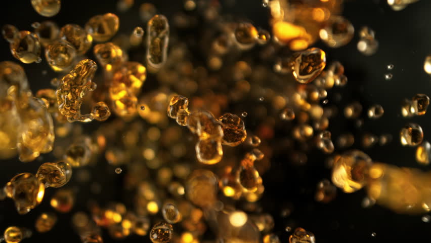 Super Slow Motion Shot of Flying Golden Liquid Drops Towards Camera on Black Background at 1000fps.