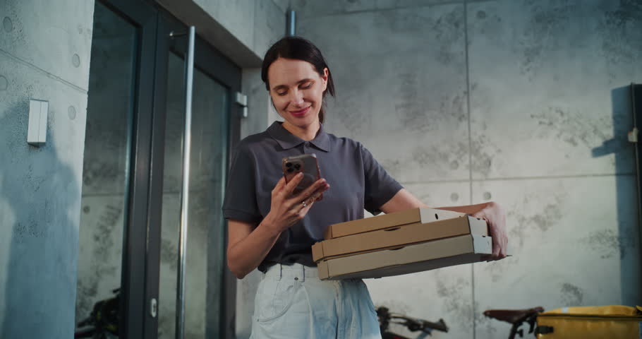 Delivery Woman Standing near Office Building with Pizza in Cardboard Boxes, Notifying Client by Phone about Successful Delivery. Woman Working in Pizza Delivery Service, Delivering Restaurant Food.