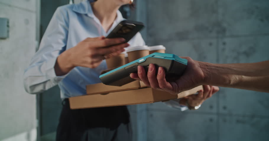 Delivery Man Giving Payment Terminal to Businesswoman after Successful Pizza Delivery to Office Building. Woman Holding Food from Restaurant, Paying for Order Contactless Using Smartphone. Close Up.