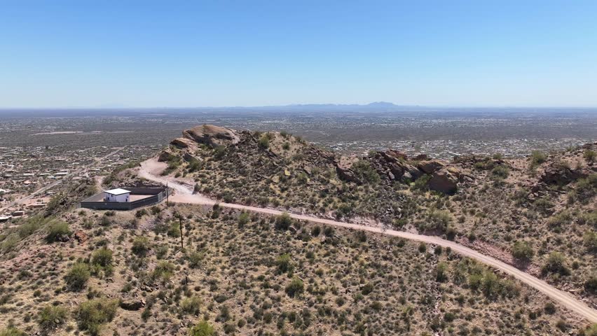 Aerial view of the rugged Superstition Mountain range with sparse desert vegetation and winding dirt trails under a clear blue sky, Apache Junction, Arizona, United States.