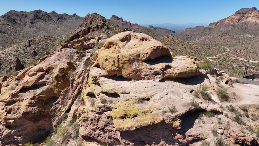 Aerial view of the Superstition Mountains with arid desert vegetation, rugged terrain, and a man-made structure, Apache Junction, Arizona, United States.
