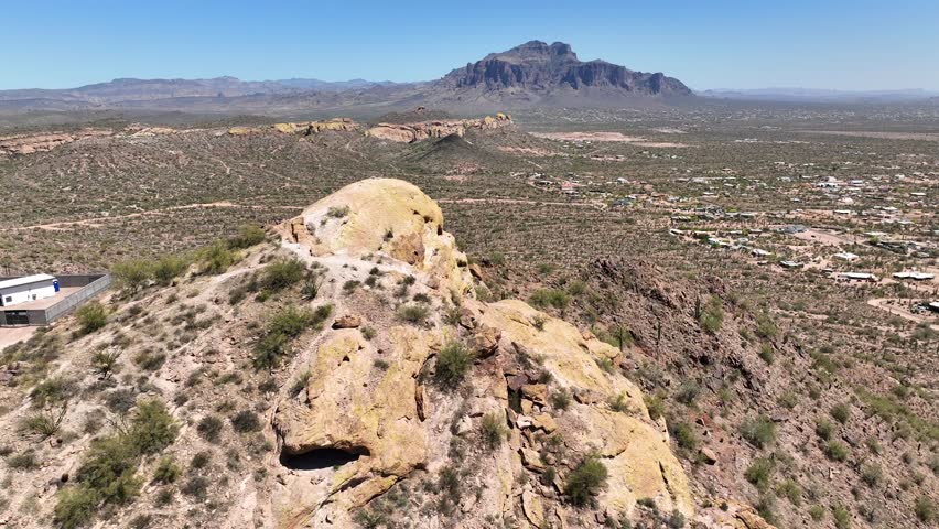 Aerial view of rugged Superstition Mountains casting shadows over the arid landscape, with sparse vegetation and rocky outcrops, Apache Junction, Arizona, United States.