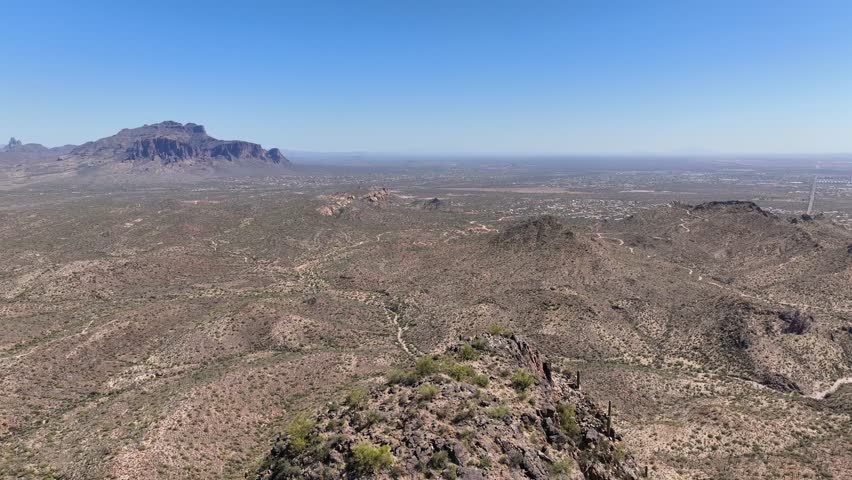 Aerial view of the rugged Superstition Mountains under a clear blue sky, casting shadows across the arid landscape, Apache Junction, Arizona, United States.