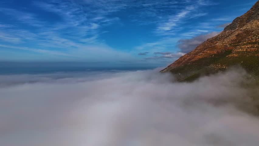 Aerial view of mountains piercing through a sea of fluffy white clouds under a bright blue sky, creating a dreamy landscape, Cape Town, Western Cape, South Africa.