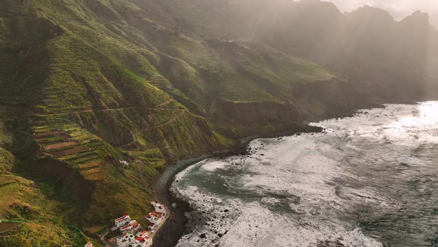Aerial view of the rugged, verdant mountains of Anaga Rural Park meeting the dark, rocky coastline and turquoise ocean waters, Santa Cruz de Tenerife, Canary Islands, Spain.