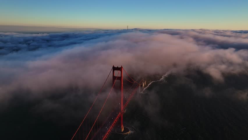 Aerial view of Golden Gate Bridge piercing through the dense fog, with a glimpse of the city skyline in the background, San Francisco, California, United States.