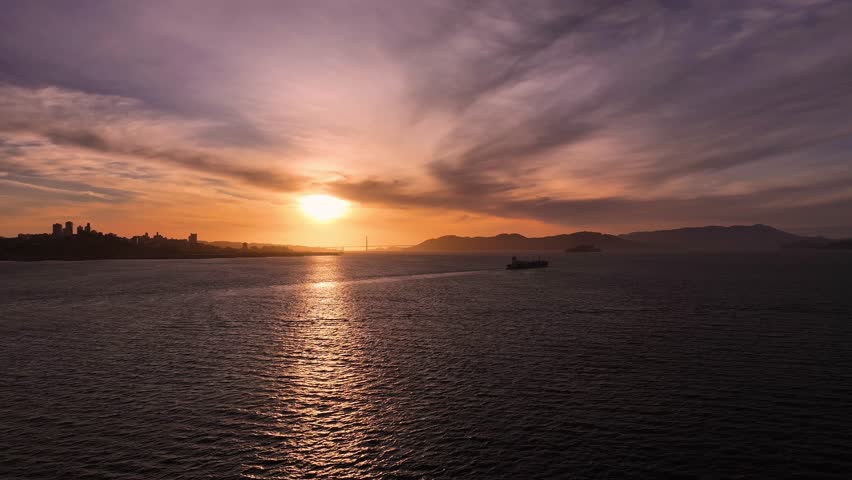 Aerial view of the Golden Gate Bridge, shrouded in a dusky haze as the sun sets over the tranquil waters, casting a golden glow on the skyline, San Francisco, California, United States.