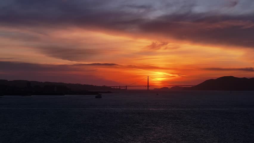 Aerial view of the Golden Gate Bridge silhouetted against a vibrant sunset, casting a warm glow over the tranquil waters, San Francisco, California, United States.