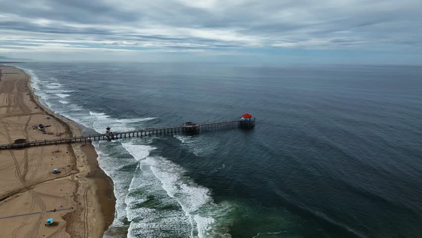 Aerial View of Huntington Beach pier extending into the ocean, waves crash onto the shore with a city scape in the horizon, Huntington Beach, California, Country.