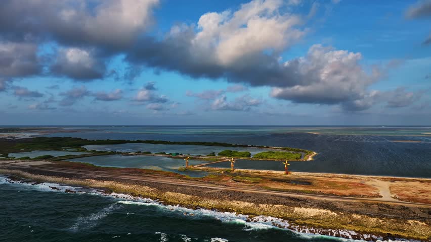 Aerial View of a rugged coastline with waves crashing against the shore, contrasting with the calm lagoons.Three windmills stand against the blue sky in Bonaire, Bonaire, Caribbean Netherlands.