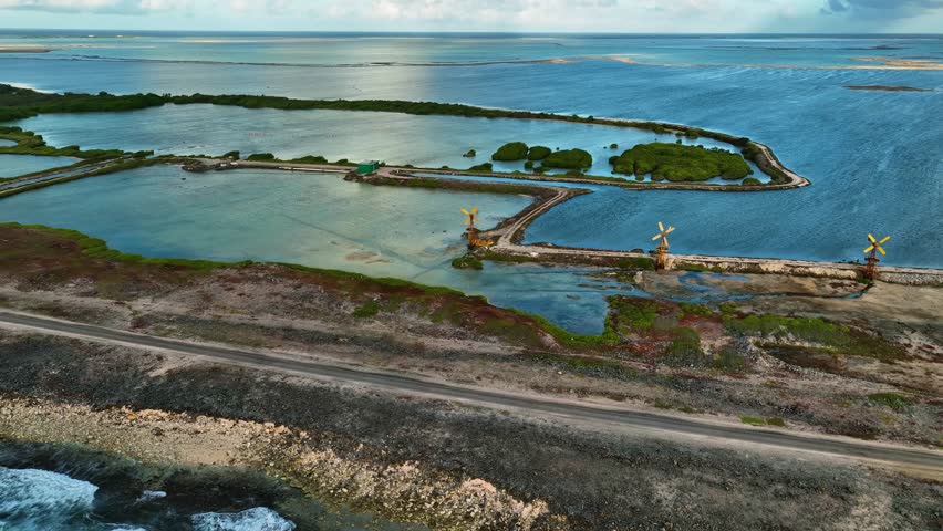 Aerial View of coastal scene showing windmills along a road separating calm turquoise waters, Bonaire, Bonaire, Caribbean Netherlands, a tranquil seascape.
