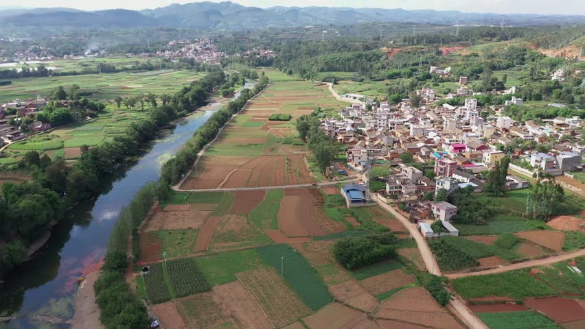 Aerial view of a river flowing through farmland and a village, creating a vibrant contrast between the natural elements and the human settlement, Kunming, Yunnan, China.