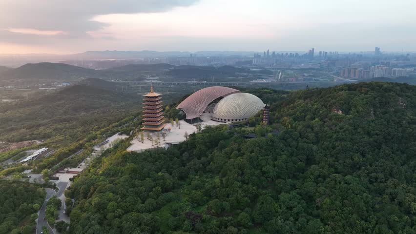 Aerial view of the majestic pagoda and the Nanjing International Expo Center nestled amidst lush green hills, contrasting with the distant cityscape, Nanjing, Jiangsu, China.