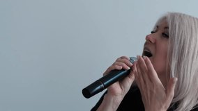 Portrait of smiling beautiful middle-aged blonde woman singing a song into a microphone on a white background, concept vocal lessons, woman singing into a microphone karaoke - Powered by Shutterstock - Get 15% off with code: PIKWIZARD15