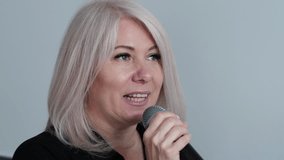 Portrait of smiling beautiful middle-aged blonde woman singing a song into a microphone on a white background, concept vocal lessons, woman singing into a microphone karaoke - Powered by Shutterstock - Get 15% off with code: PIKWIZARD15