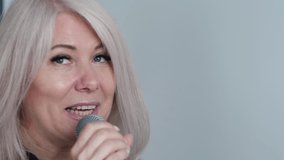 portrait of cheerful middle aged caucasian blonde woman singing song into microphone, singer rehearsing or performing song on performance, white background, concept vocal lessons - Powered by Shutterstock - Get 15% off with code: PIKWIZARD15
