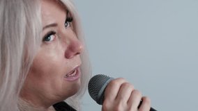 portrait of cheerful middle aged caucasian blonde woman singing song into microphone, singer rehearsing or performing song on performance, white background, concept vocal lessons - Powered by Shutterstock - Get 15% off with code: PIKWIZARD15