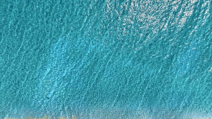 Aerial view of sea surface with reflected sunlight. Turquoise water ripples background texture on sea coast. Mediterranean waves on bright sunny day. Water landscape.