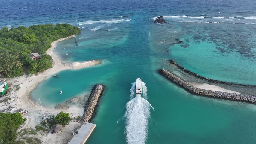 Aerial view of a boat cruising through the turquoise waters near Bileffahi, with lush green islands and rocky formations visible, Bileffahi, Shaviyani Atoll, Maldives.