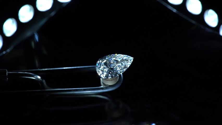 A gleaming pear-shaped diamond meticulously held on a specialized gem holder under precise lighting, highlighting its exceptional brilliance and unique cut.