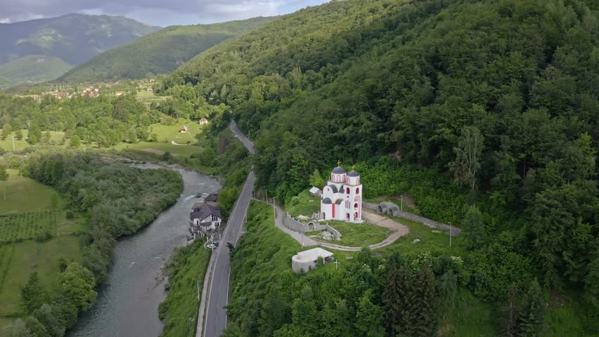 Aerial view of a church, nestled among verdant trees, stands proudly above a winding river and road, a tranquil scene, Боботов Кук, Montenegro.