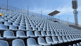 Rows of empty blue plastic stadium seats sit under a bright sky, with a single yellow seat standing out among the uniform pattern - Powered by Shutterstock - Get 15% off with code: PIKWIZARD15