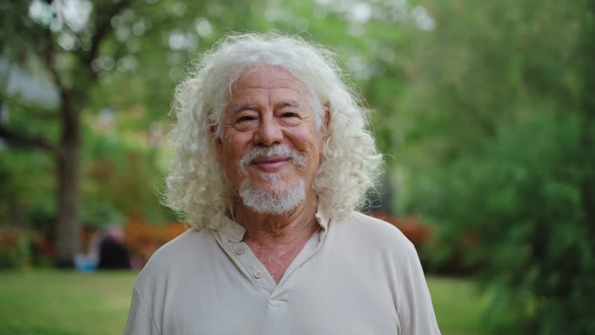 Portrait of happy senior man laughing in park. Funny grandpa with long curly hair. Retirement and happiness