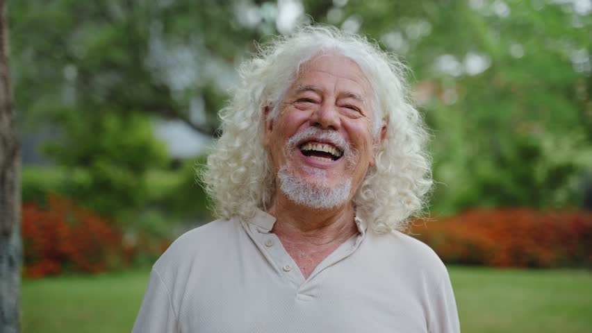 Portrait of happy senior man laughing in park. Funny grandpa with long curly hair. Retirement and happiness