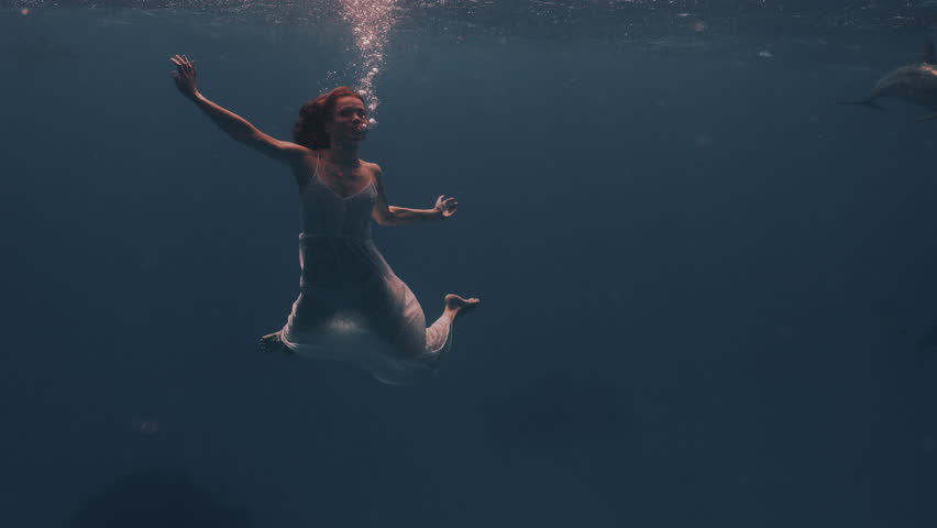 Beautiful young woman swimming underwater with dolphins in pristine blue ocean water, amazing snorkeling adventure. Armature freediver girl diving in red sea with bottlenose dolphins. Travel concept