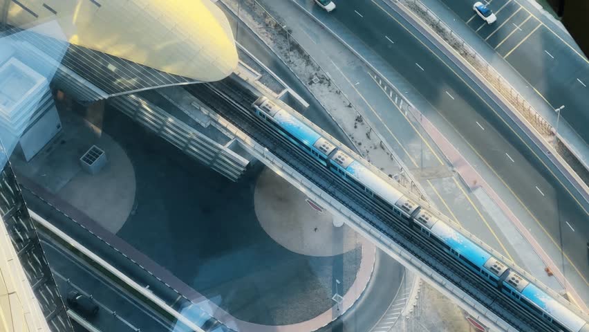 Elevated metro train passing arriving at modern architectural station along highway traffic with cars, taxi cabs driving