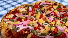 Close up macro dynamic view holding a slice of colorful vibrant pizza with red, green, yellow peppers, mushrooms, vegetables, pineapple, onions, and pepperoni toppings on a picnic table background - Powered by Shutterstock - Get 15% off with code: PIKWIZARD15
