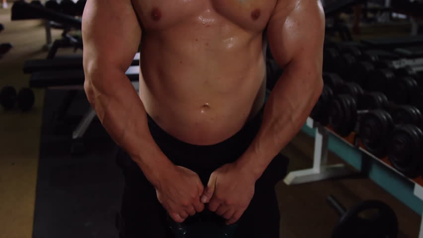 Man gripping 20kg kettlebell at waist and lifting toward chest to strengthen shoulders in gym. Strength, fitness, training, characterization, motivation, power, determination