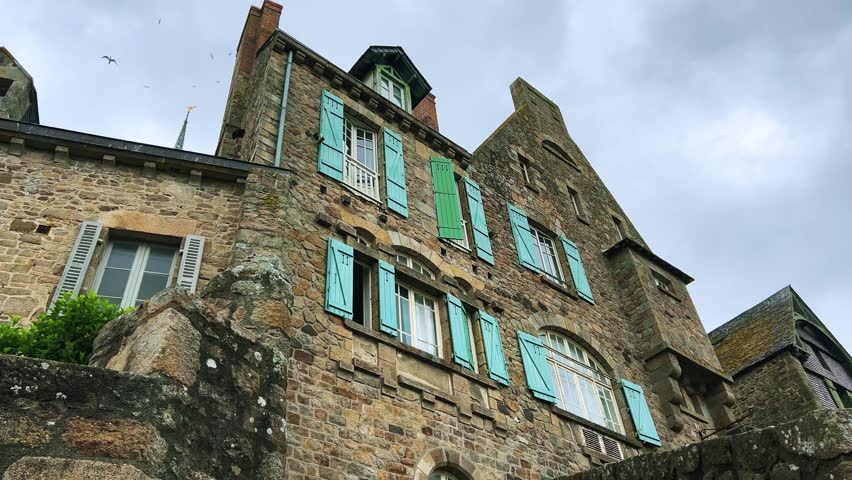 Old stone house with shuttered windows on a cloudy spring day in Mont Saint Michel Abbe, Normandy, France.