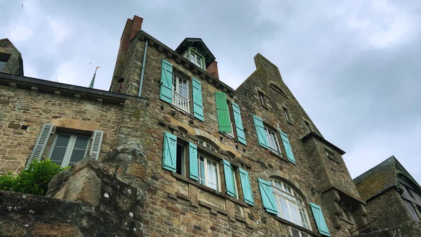 Old stone house with shuttered windows on a cloudy spring day in Mont Saint Michel Abbe, Normandy, France.