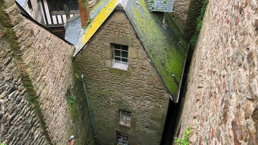 Top view from the walls of Mont Saint Michel Abbey to the island's ancient stone houses and rooftops on a cloudy spring day, Normandy, France.