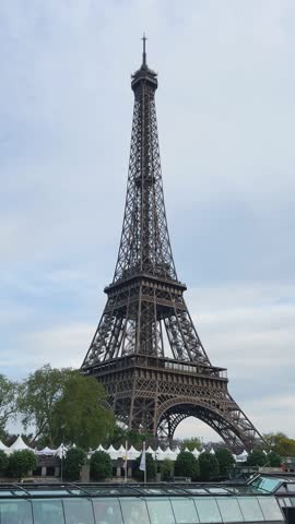 View of the left bank of the Seine River, the Eiffel Tower, ferries on the river, the Quai Jacques-Chirac embankment on a cloudy spring day in the 7th arrondissement of Paris, France. Vertical video.