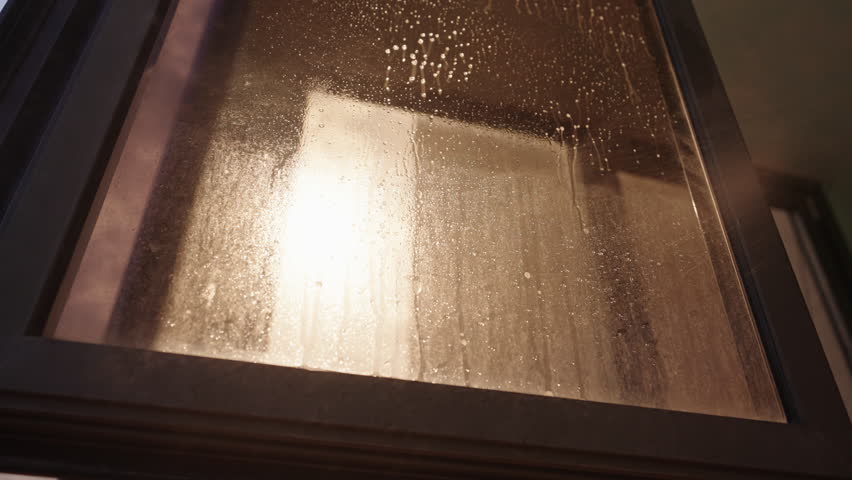 Low-angle view of cleaning service employee spraying window cleaner and using microfiber towel to wipe dirty window on background of sunlight, cleaning and maintaining fresh hygienic environment.