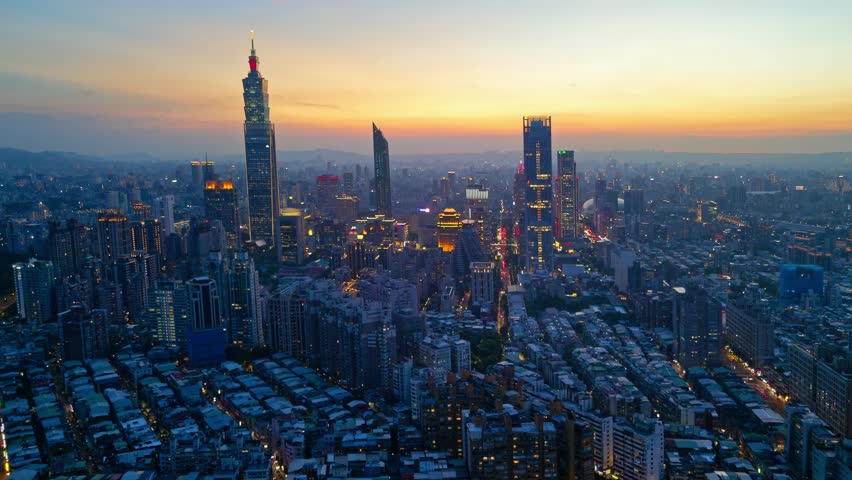 Aerial hyperlapse of Downtown Taipei at dusk, the vibrant capital city of Taiwan, with 101 Tower standing out amid skyscrapers in XinYi Commercial District and city lights dazzling under twilight sky