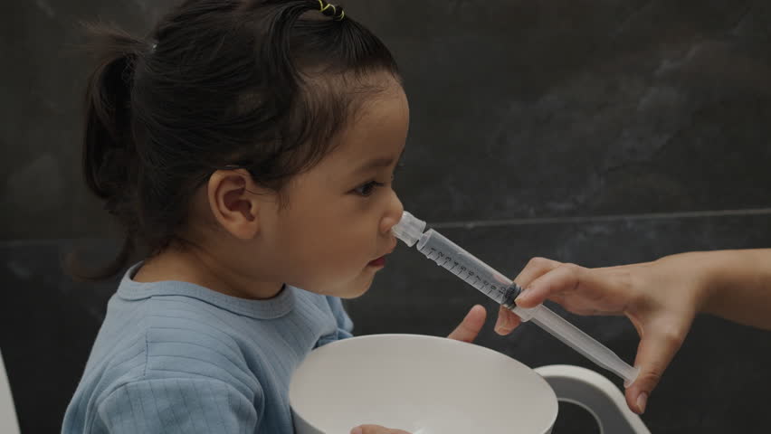 mother making nasal wash for toddler girl with syringe and saline. cleaning nose