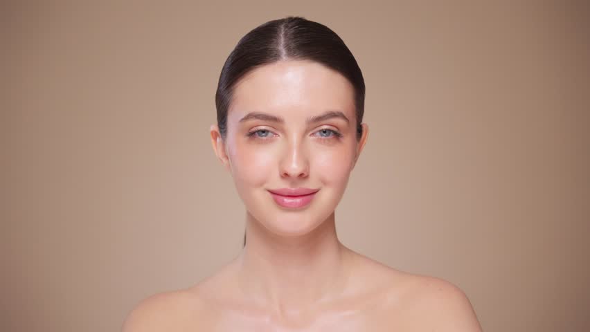 Beautiful Young Woman Touches Her Perfect Face. Natural Cosmetic Skincare Products. Woman demonstrate moisturizing facial care. Elevating Close-up Portrait with Isolated Background. Slow motion