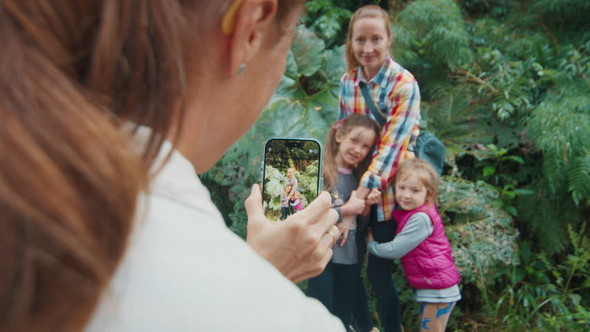 Family hiking in the wet tropical forest with lush vegetation. Woman takes picture of the family with kids in the forest